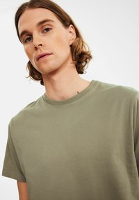 Olivengrøn bomuld T-shirt med rund halsudskæring og korte ærmer, der har en glat tekstur og en afslappet pasform.