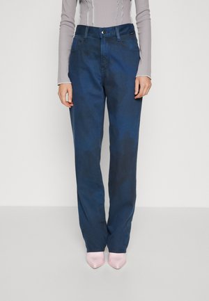 Dunkelblaue weit geschnittene Jeans aus Denim, mit hoher Taille, Vorderaschen und Knopfverschluss, kombiniert mit rosa High Heels.