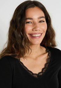 Haut noir à manches longues avec un bord en dentelle à volants le long du décolleté en V, présentant un tissu doux et une coupe ajustée.