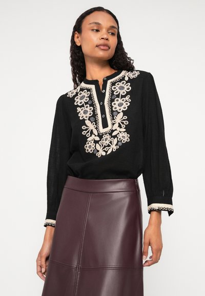 Čierny top s kvetinovou výšivkou v béžovej a modrej farbe, s výstrihom a dlhými rukávmi. Spárovaný s bordovými koženými sukňami.