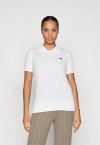 Polo a maniche corte bianca in maglia con orlo a coste, caratterizzata da un motivo a treccia e un accento del logo nero sul petto.