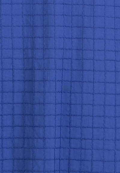 Tissu bleu avec un motif en grille matelassé composé de carrés surélevés cousus, présentant de légers plis et une texture.