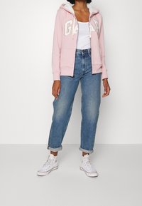 Felpa rosa con il logo "GAP", cappuccio foderato in pile, tasche frontali, abbinata a jeans blu a vita alta e sneakers bianche alte.