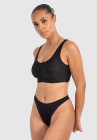 Sujetador deportivo negro con tirantes anchos y una textura suave, combinado con un tanga negro a juego. Diseño simple, sin hardware visible ni patrones.