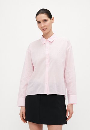 Light pink long-sleeve shirt with a button-up collar, featuring vertical stripes and small embroidered dots. Worn over a black skirt.