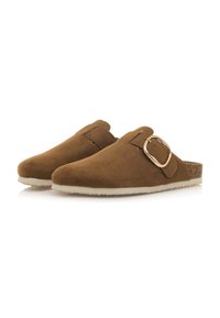 Sabots en daim marron avec une semelle blanche plate, dotés d'une boucle sur le côté et d'une touche de liège sur le talon. Texture lisse.