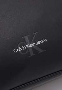 Svart lommebok i faux skinn med preget tekstur og trykt "Calvin Klein Jeans"-logo i hvit, med en subtil grå aksent på "CK."