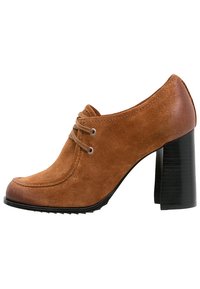 Zapato de tacón alto de ante marrón con puntera redondeada, con cordones y un tacón de bloque negro texturizado. Superficie lisa y diseño elegante.