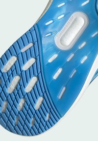 Kenkäpohja, jossa on sininen kuminen pitoalue kuvioiduin pintakuvioin. Keskiosassa on valkoinen Torsion System -komponentti.