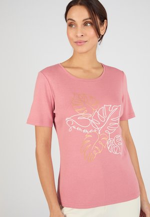 Vrouw die een roze T-shirt met korte mouwen draagt met gele en witte tropische bladdesigns en het woord "summer" geschreven over de voorkant.