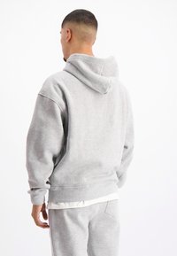 Grijze hoodie van zacht, textuurstof. Heeft een grote capuchon, losse pasvorm en ribgebreide manchetten. Draag met bijpassende joggerbroek.