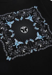 Zwarte T-shirt met een centraal decoratief patroon van blauwe vlinders, ingewikkelde bloemdessins en het Tomorrowland-logo in het midden.