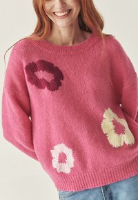 Pulover tricotat roz cu broderie florală în nuanțe de crem și burgund. Prezintă un guler rotund și mâneci lungi, lejere.