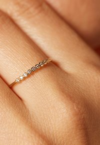 Gouden ring met een rij afwisselende heldere en zwarte edelstenen die langs de band zijn gezet, tentoongesteld op een textuurrijke hand.