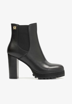 Botte noire en cuir à la cheville avec des panneaux latéraux élastiques, talon épais, semelle en caoutchouc avec motifs antidérapants, et un logo doré sur l'arrière.