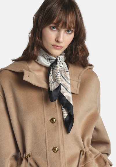 Svila šal u krem boji s crnim naglascima i geometrijskim uzorcima, nošen s teksturiranim bež vunenim kaputom s zlatnim gumbima i kapuljačom.