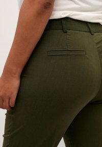 Pantalon vert olive à texture lisse, avec une poche passepoilée à l'arrière, une taille mi-haute et une coupe ajustée.