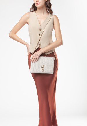 Top senza maniche beige con bottoni; gonna lunga color ruggine; borsa leggera grigia testurizzata con catena dorata e accento con logo.