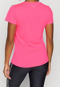 Jasně růžové sportovní tričko s krátkými rukávy, kulatým výstřihem a hladkou texturou. Na horní části zad je umístěno logo.
