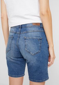 Džínové šortky v středně modré barvě, s klasickým designem pěti kapes, jemným popraskáním a koženým značkovým štítkem na pase.
