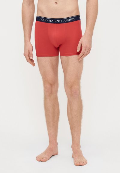 Raudonos medvilnės boxer tipo kelnaitės su tamsiai mėlynu elastiniu juosmeniu, ant kurio yra „POLO RALPH LAUREN“ logotipas. Prigludęs dizainas, lygi tekstūra ir ilgis iki vidurio šlaunies.