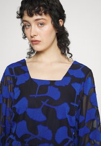 Vestido de tecido preto transparente com um design de folha de ginkgo bordada em azul, apresentando um decote quadrado e mangas longas.