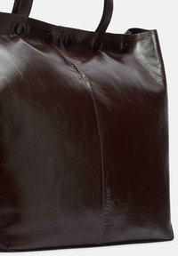 Ciemnobrązowa skórzana torba na ramię z podwójnymi uchwytami, widocznymi szwami i czarnymi napami wzdłuż górnej krawędzi.