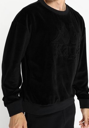 Czarna welurowa bluza z okrągłym dekoltem i długimi rękawami. Na przodzie znajduje się teksturowane logo "Kappa". Miękki, gładki materiał.