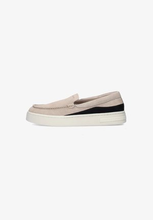 Zapato slip-on beige claro hecho de ante con un panel de acento negro. Presenta una suela blanca gruesa y un detalle de costura en la parte superior.