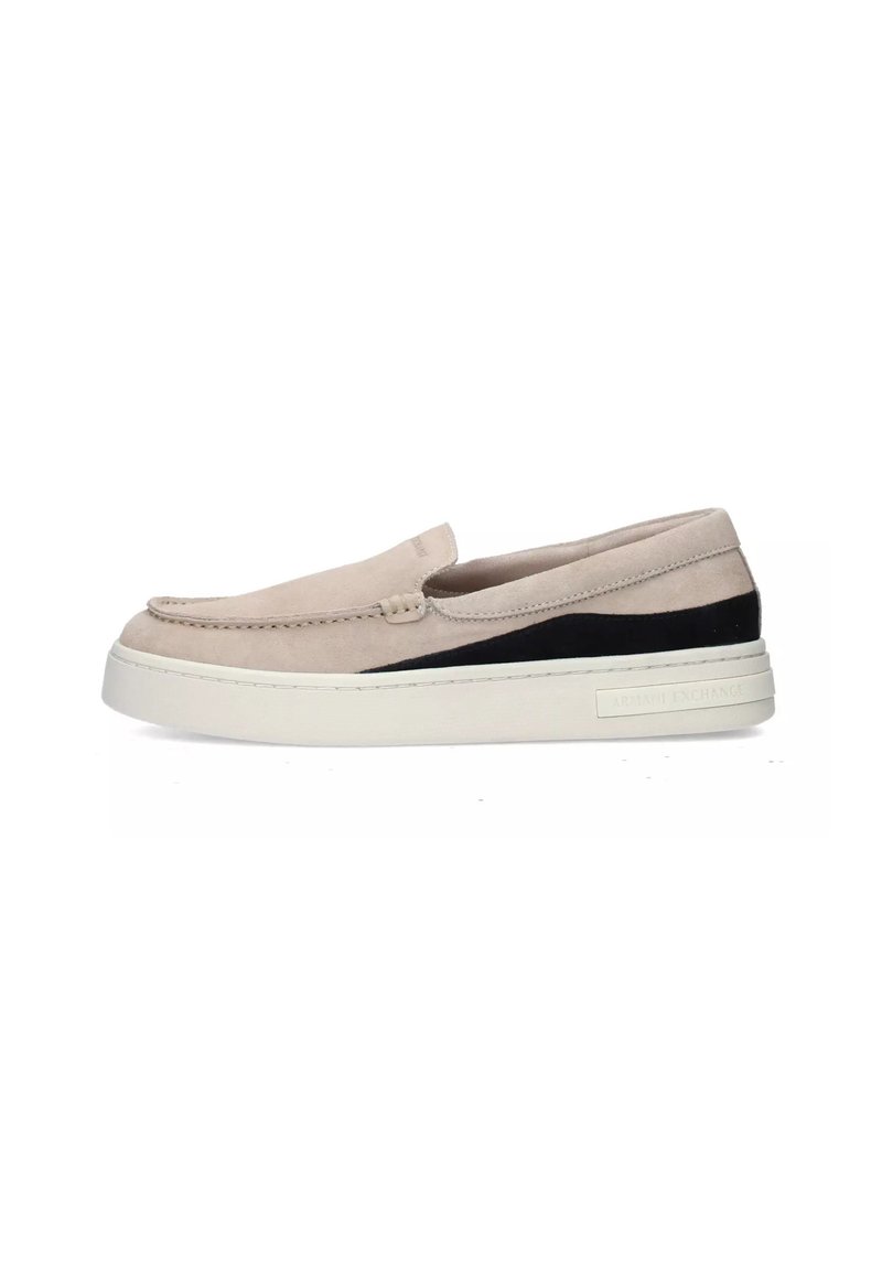Scarpa slip-on beige chiaro in suede con un pannello accentato nero. Presenta una suola bianca spessa e dettagli di cucitura lungo la parte superiore.