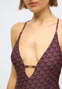 Maillot de bain à décolleté plongeant en bordeaux profond avec un motif cursif rose clair. Bretelles fines ajustables et détail en métal doré à la taille.