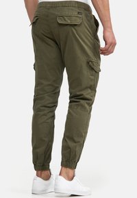 Pantaloni cargo verde măsliniu cu talie și manșete elastice, având multiple buzunare și un material neted, ușor din bumbac.