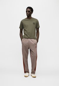 Λαδί πράσινη μπλούζα με γραφικό κάκτου, σε συνδυασμό με καρό παντελόνι με κόκκινες πλευρικές ρίγες και λευκά αθλητικά παπούτσια. Γυαλιά ηλίου ολοκληρώνουν την εμφάνιση.