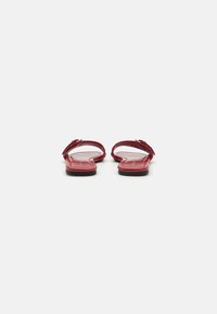 Red flat sandals with two straps and a buckle detail, smooth texture, open back, and a minimalist black sole.