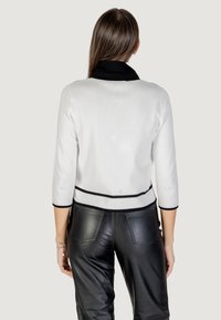 Maglione bianco con colletto e polsini neri, caratterizzato da un bordo nero in vita. Abbinato a pantaloni in pelle neri, che mostrano una superficie liscia.