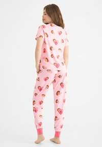 Ljusrosa pyjamasset med kort ärm och tapered byxor. Tyget visar ett mönster av igelkottar och hjärtan, med rosa mudd.