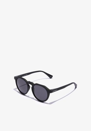 Mustat aurinkolasit, joissa on oktaalinen kaksoisrakenne, harmaat linssit ja suorat sakarat. Merkin "HAWKERS" teksti on painettu sivulle. Valmistettu Espanjassa.