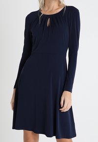 Mörkblå långärmad klänning med rund halsringning, nyckelhålsdetalj framtill, figursydd liv och utsvängd kjol i ett mjukt tyg.