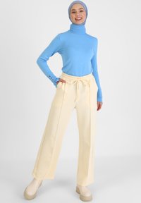 Blauwe coltrui met lange mouwen, gecombineerd met crèmekleurige wijd uitlopende broek met een elastische tailleband en twee zijzakken.