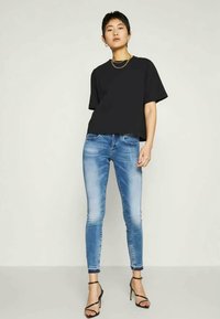Schwarzes, oversized T-Shirt, blaue Skinny-Jeans mit ausgewaschenen Stellen und schwarzen Riemchen-Heels. Einfaches Design, kurze Ärmel und glatte Stofftextur.