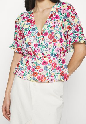 Mujer con blusa de flores coloridas con escote en V, mangas cortas abullonadas y cintura ajustada, combinada con una falda blanca.