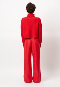 Roter Cropped-Pullover mit hohem Kragen, kombiniert mit hoch taillierten, weit geschnittenen roten Lederhosen. Glatte Textur mit minimalen Designdetails.