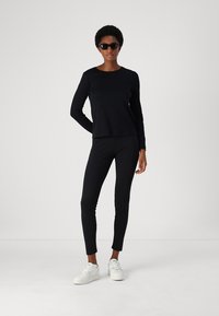 Zwarte lange mouwen top en strakke leggings van zacht materiaal, gecombineerd met witte sneakers. De outfit heeft een schone, minimalistische uitstraling.