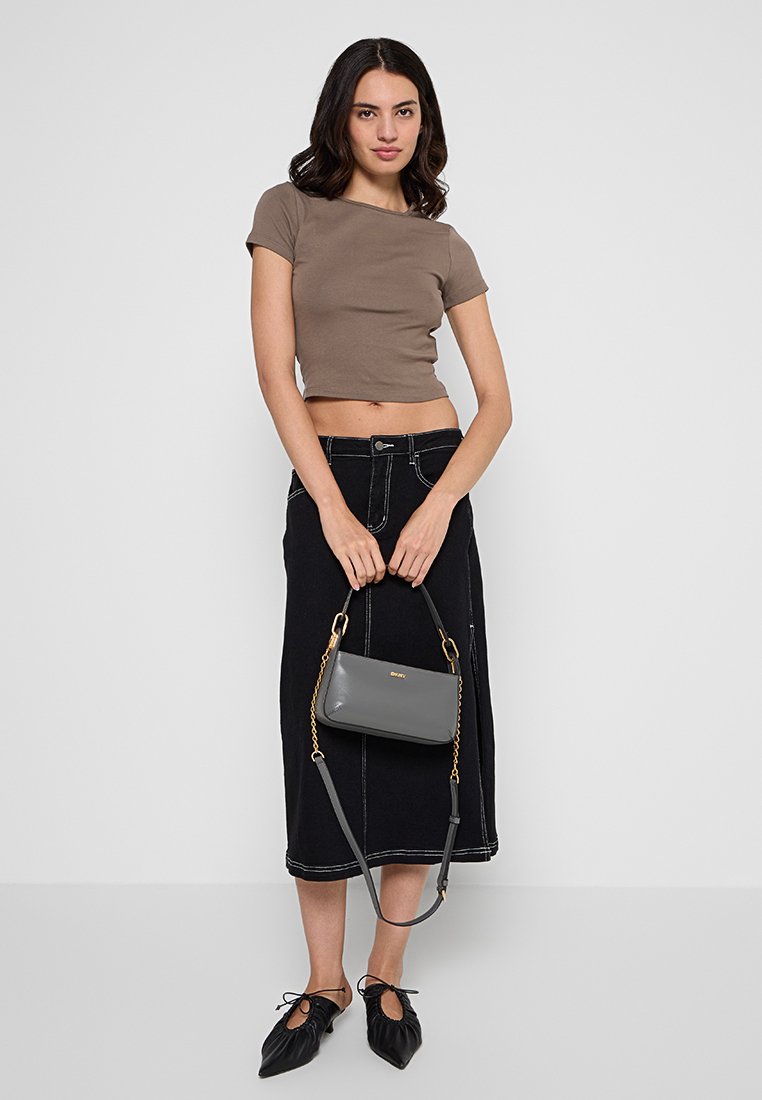 Graue Lederhandtasche mit einem goldenen Kettenriemen, gehalten von einer Person, die ein braunes, kurzes Oberteil und einen schwarzen Jeansrock trägt. Das Outfit ist einfach und modern.