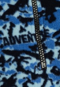 Chaqueta de forro polar en azul y negro, con cremallera, un patrón de camuflaje con el texto "ADVENTURE" y una textura suave.