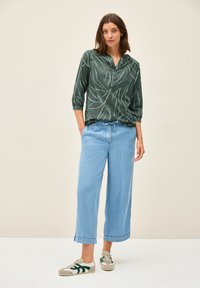 Blusa leggera con motivo a foglie verdi e maniche a tre quarti, abbinata a pantaloni in denim azzurri a taglio largo e sneakers casual.