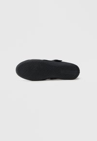 Sapato preto com sola de borracha texturizada, tira ajustável e material superior liso. Design minimalista com detalhes funcionais.