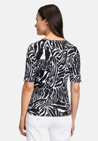 Top a maniche corte con motivo zebra bianco e nero, scollatura rotonda, tessuto morbido e silhouette aderente. Pantaloni bianchi visibili sotto.
