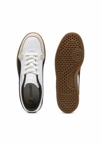Paire de baskets Puma blanches et noires vues de dessus et de la semelle avec une semelle extérieure en caoutchouc brun texturé et des lacets blancs.