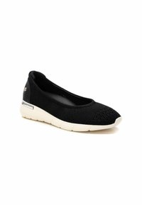 Zapato negro tipo slip-on con parte superior de malla transpirable, puntera redondeada, detalles texturizados y suela de goma blanca con un acento metálico en el talón.